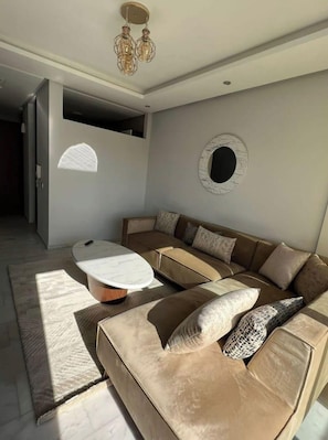 Un salon moderne avec un canapé d’angle, une table basse ronde et un miroir circulaire original fixé au mur.