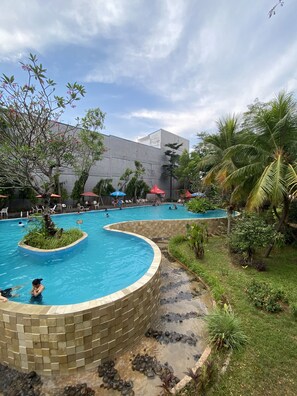 A pool area with multiple swimming pools, surrounded by palm trees and greenery. - Ispi Hotel Cikarang Festival (Cikarang)