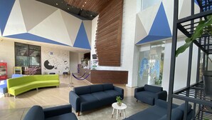 Un vestíbulo moderno con un sofá verde curvo, sillones azul oscuro y una recepción.