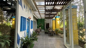 Un espacio al aire libre cubierto con mesas y sillas, un muro de cristal y una pared verde con plantas.