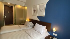 Habitación de hotel con dos camas, un escritorio, una silla y una pared decorada en azul.