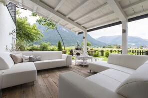 Un espace extérieur aménagé avec des meubles de jardin, comprenant des canapés blancs et une petite table ronde, et offrant une vue sur un paysage montagneux.