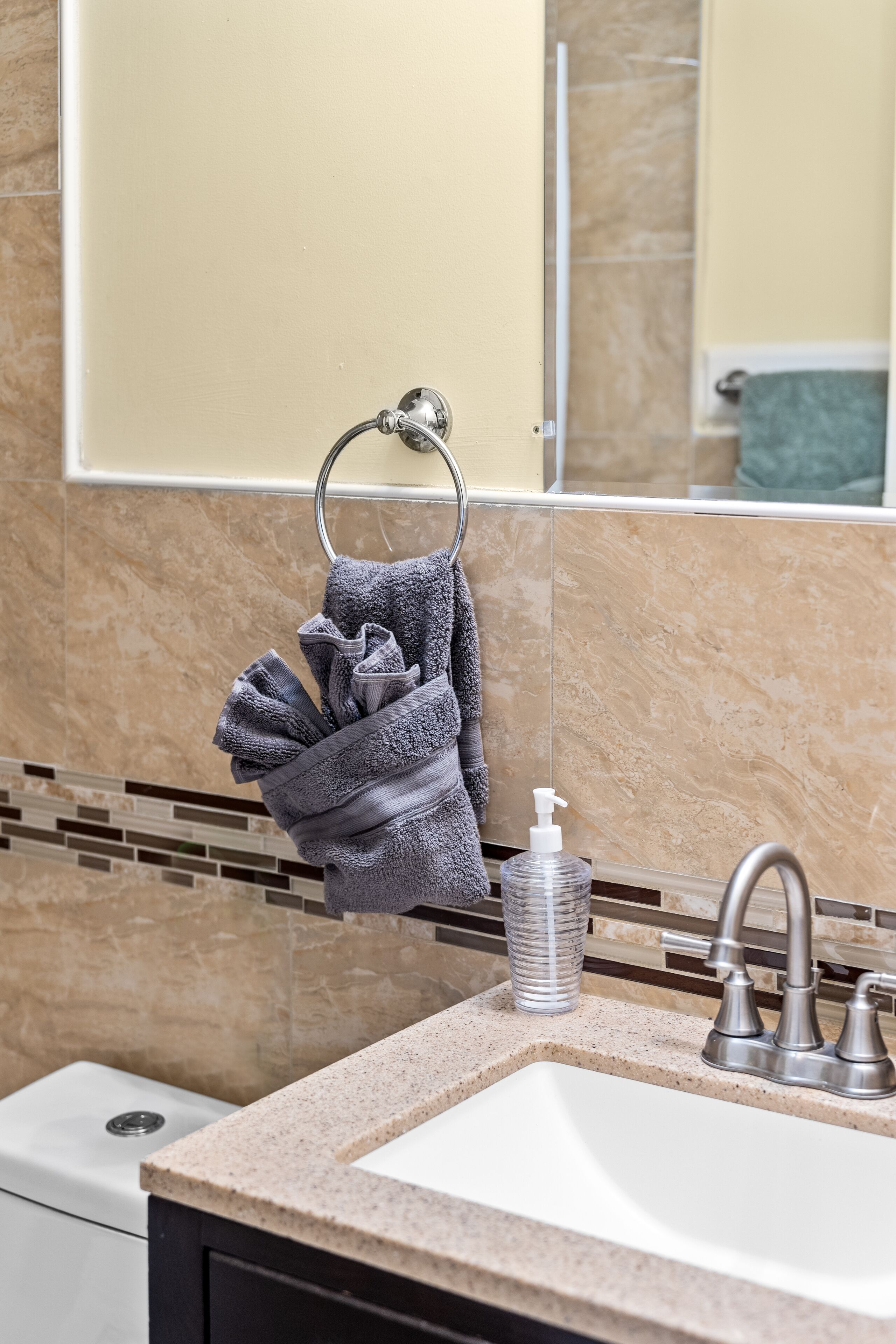 A bathroom with a sink, mirror, towel rack, and soap dispenser.