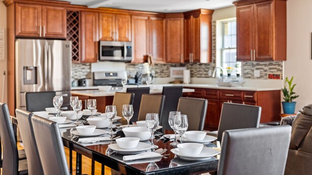 Una cocina moderna con armarios de madera, electrodomésticos de acero inoxidable y una zona de comedor preparada para seis personas con una mesa de mármol.