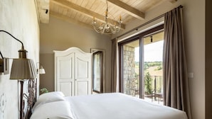 Ein Schlafzimmer mit einem großen Bett, einer Kristallleuchtre, einem weißen Kleiderschrank und Blick ins Freie durch eine Glastür.