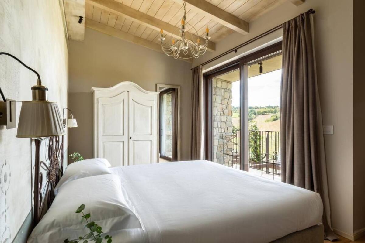 Une chambre dotée d’un grand lit, d’un lustre, d’une armoire blanche et offrant une vue sur l’extérieur grâce à une porte-fenêtre coulissante.