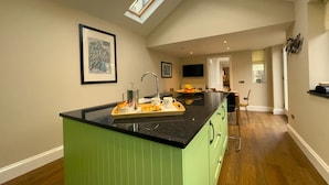 A modern kitchen with a green island, skylights, and a dining area in the background.