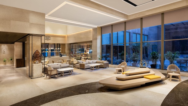 A spacious lobby with a modern design, featuring a seating area, a reception desk, and large windows offering a view of the outdoors.