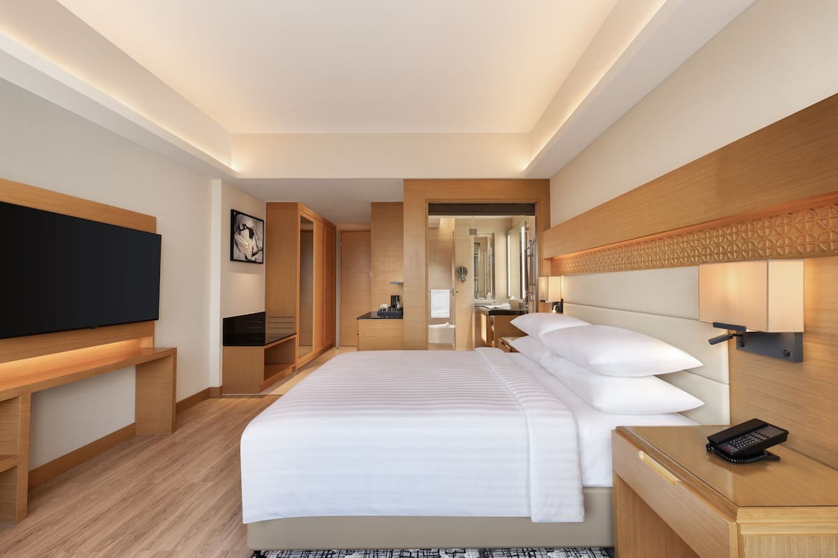 A modern hotel room with a large bed, a flat-screen TV, a wooden desk, and a walk-in closet.