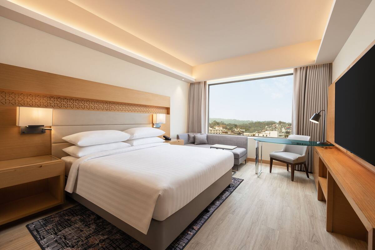 A modern hotel room with a large bed, a desk, and a view of the city.