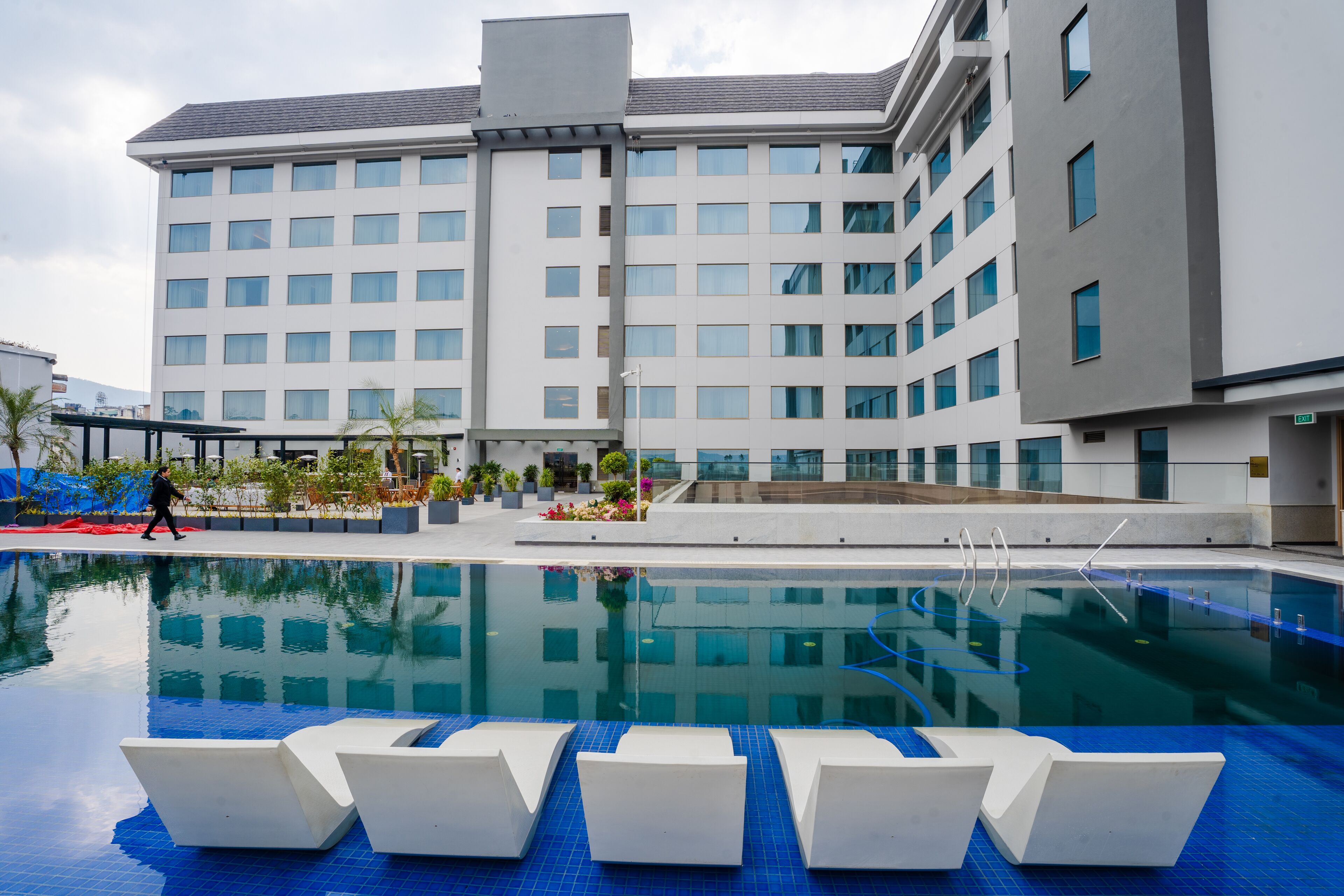 A modern hotel with a swimming pool, multiple floors, and a covered outdoor area with plants.