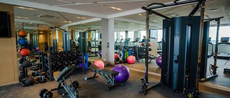 Un gimnasio con diferentes equipos de ejercicio, espejos y suelo alfombrado.