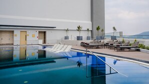 A rooftop pool with lounge chairs and a view of the city.