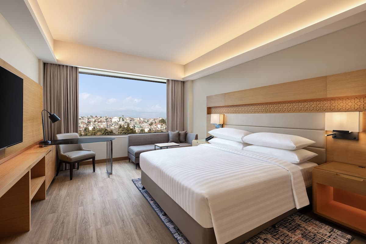 A modern hotel room with a large bed, a desk, a sofa, and a TV.