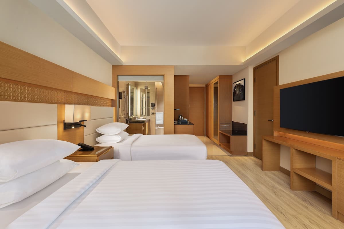 A hotel room with two beds, a TV, a desk, and a mirror.