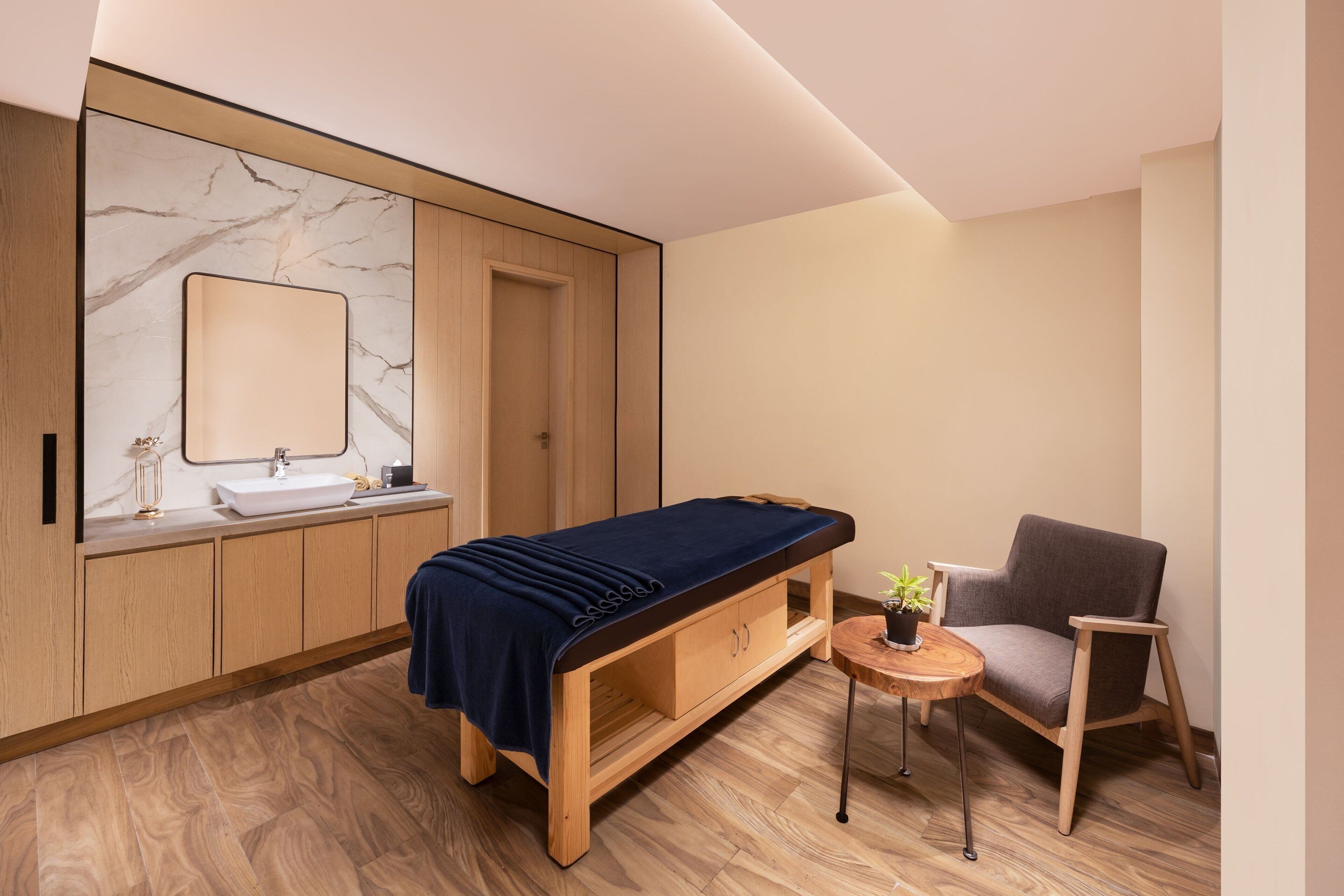 Een moderne kamer met een houten bed, een klein tafeltje met een plant, een stoel, een spiegel en een wastafel.