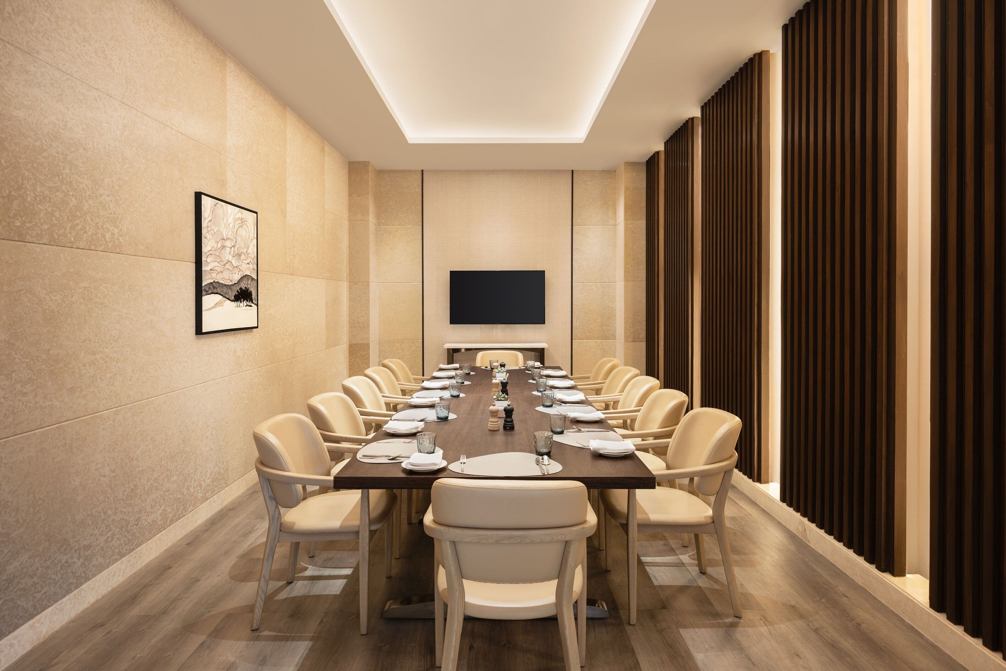 A conference room with a long table, chairs, a flat-screen TV, and a framed picture on the wall.