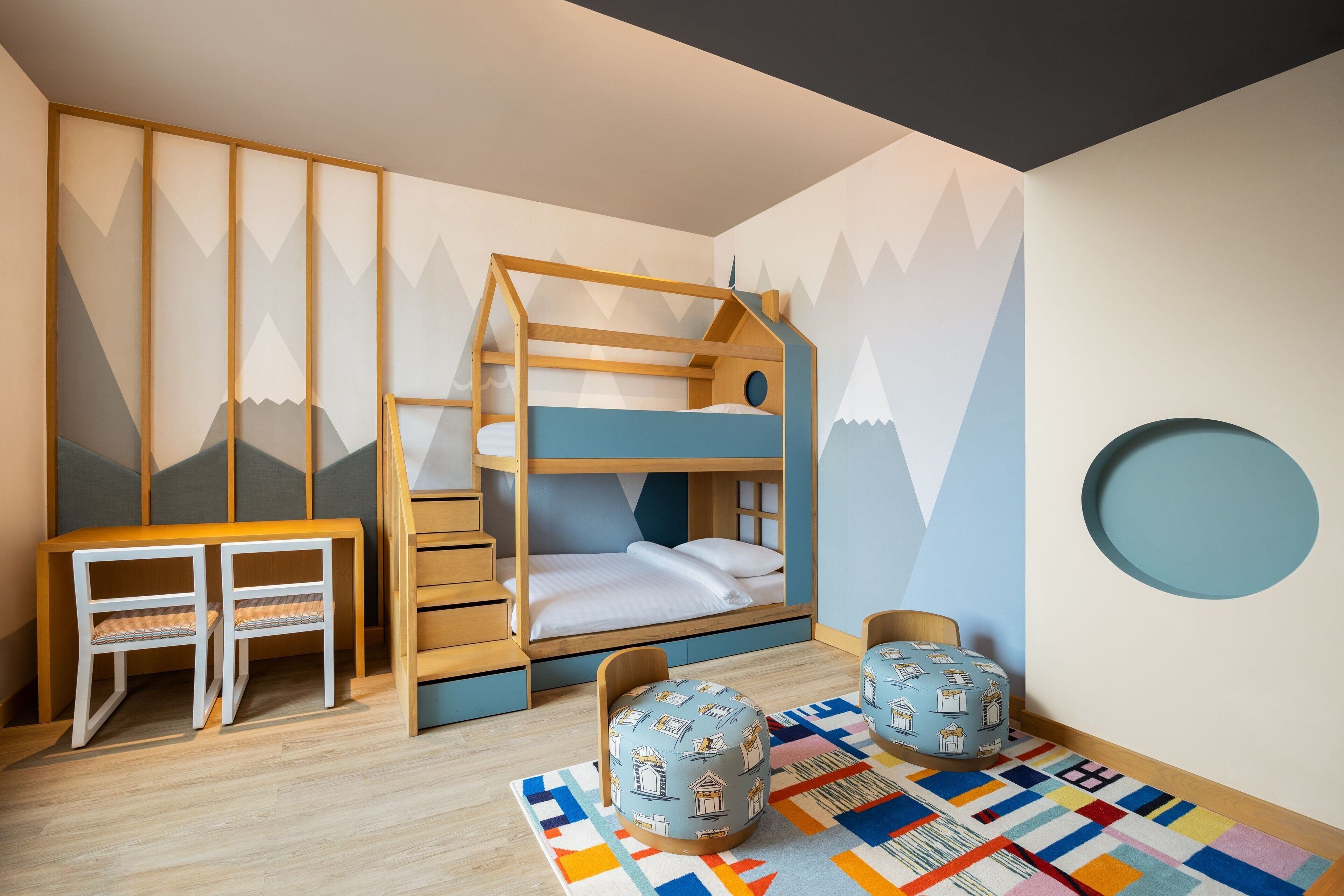 A child's bedroom with bunk beds, a desk, chairs, and a colorful rug.