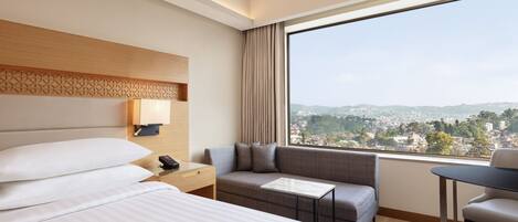 Habitación de hotel con una cama grande, un sofá, una mesita y vistas a la ciudad.