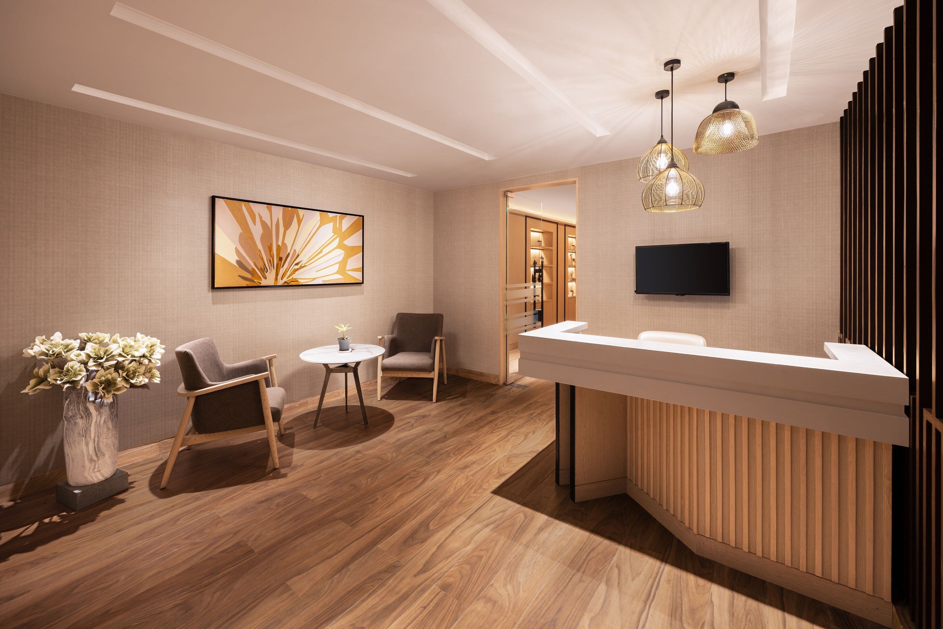 A modern reception area with a wooden reception desk, two chairs, a vase with flowers, and a large abstract painting on the wall.