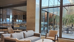 A modern lounge area with sofas, chairs, and a coffee table, large windows offering views of the outside.