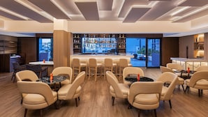 A modern bar area with a central seating arrangement, a well-stocked bar, and a view of the outdoors.