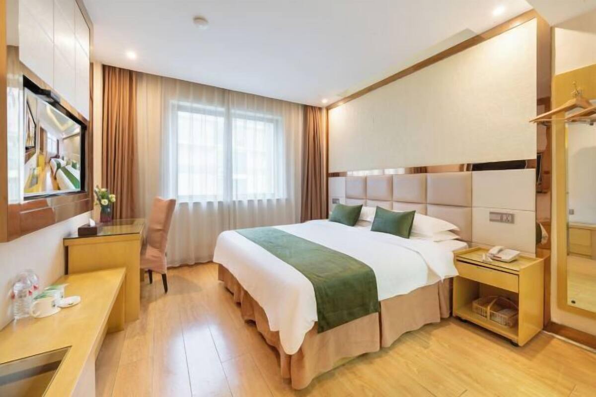 Une chambre d’hôtel comprenant un lit, des tables de chevet, un bureau, une chaise, un miroir et une fenêtre avec des rideaux.