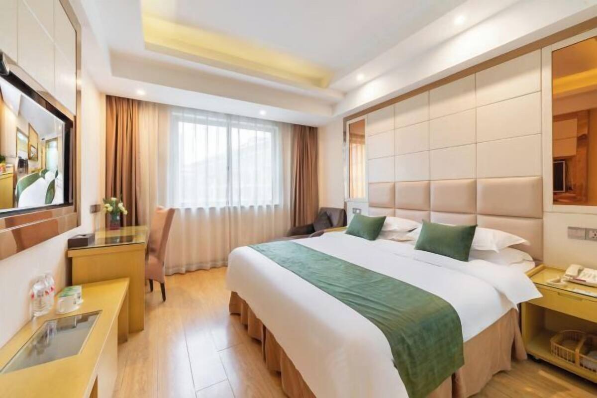 Une chambre d’hôtel avec un grand lit, un bureau, une chaise, un miroir et une fenêtre avec des rideaux.