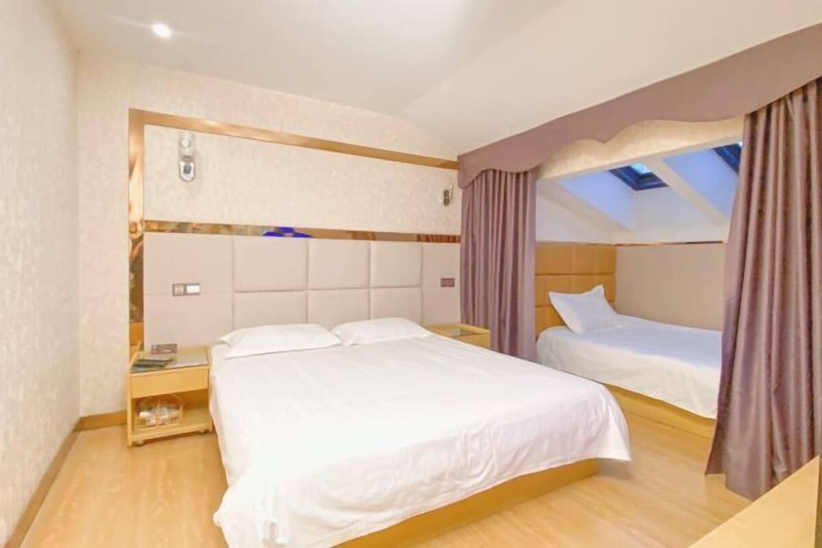 Une chambre avec deux lits, un plancher en bois, une tête de lit dotée d’un luminaire et une lucarne.