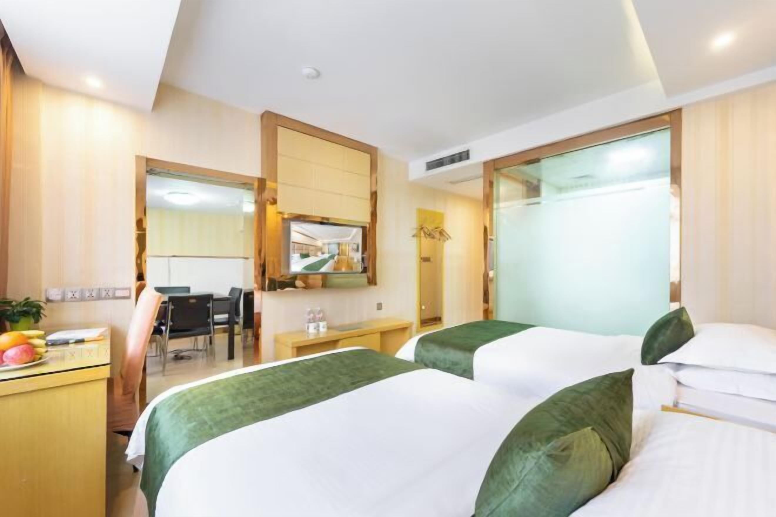 Habitación de hotel con dos camas, un escritorio, una silla, un espejo y un baño visible a través de una puerta de cristal.
