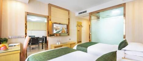 Quarto de hotel com duas camas, uma escrivaninha, uma cadeira, um espelho e um banheiro visível através de uma porta de vidro.