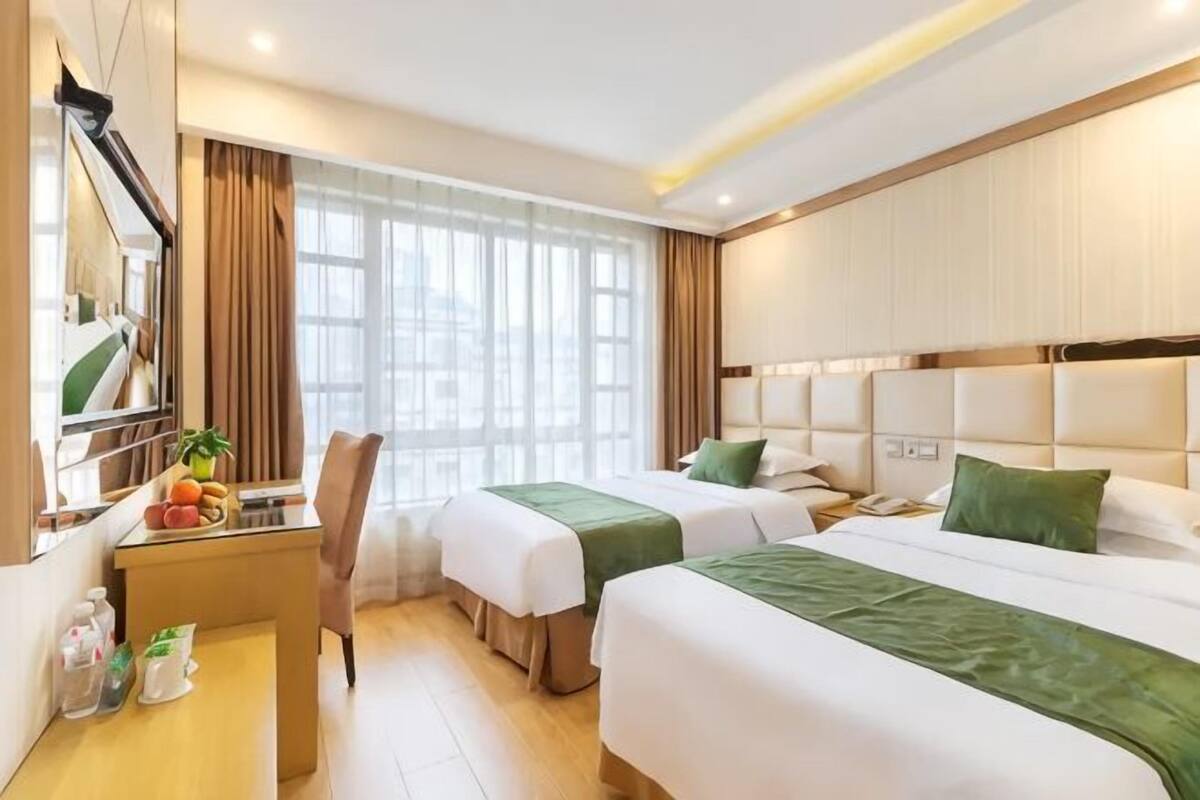 Une chambre d’hôtel avec deux lits, un bureau, une chaise et une grande fenêtre.