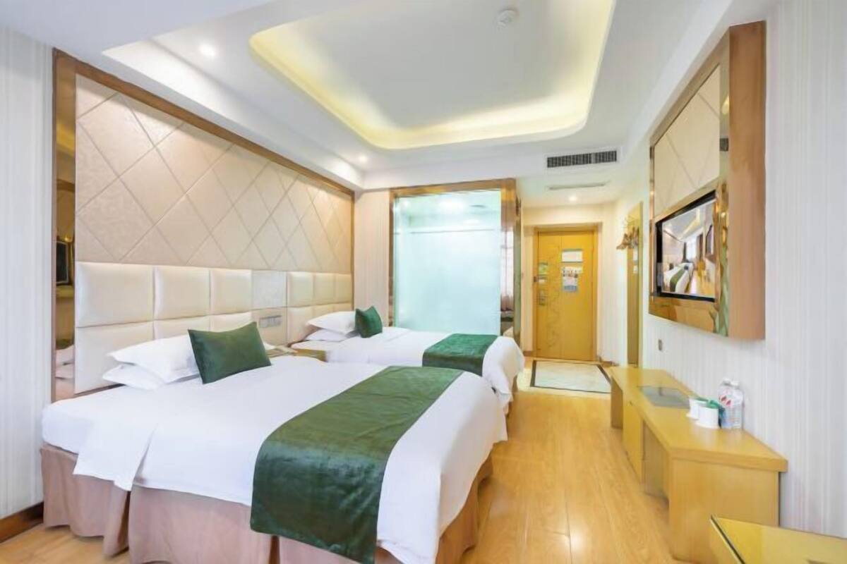 Une chambre d’hôtel avec deux lits, un plancher en bois, un comptoir de réception et un téléviseur fixé au mur.