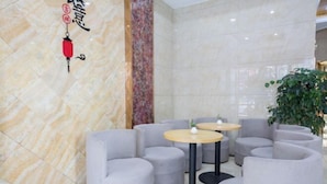 A modern lobby with marble walls, grey upholstered seating, and small round tables. - GreenTree Shell Hotel (Yiwu International Business City Changchun Accessories Specialty Street) (Yiwu)