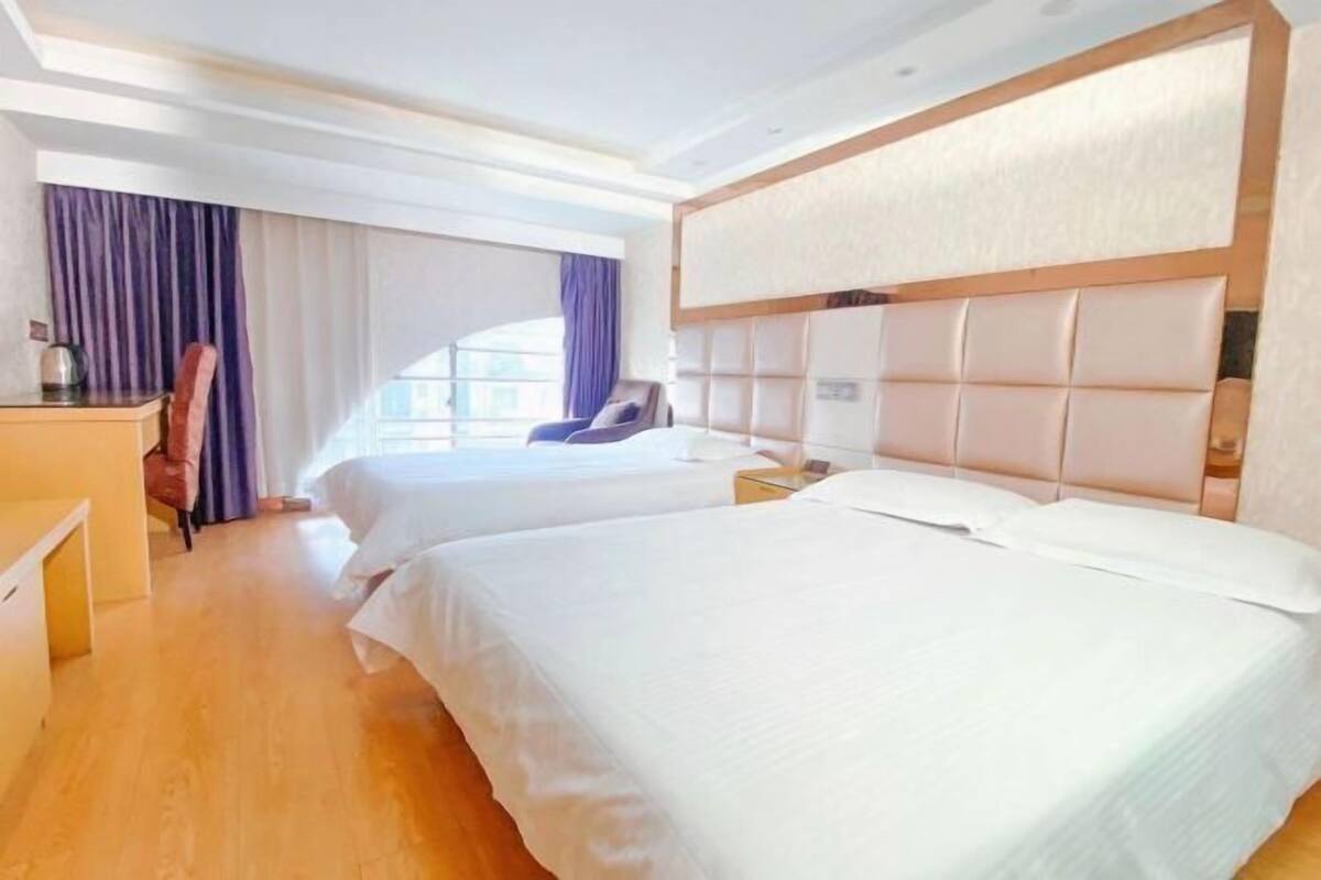 Une chambre d’hôtel avec deux lits, un bureau, une chaise et une grande fenêtre avec des rideaux.