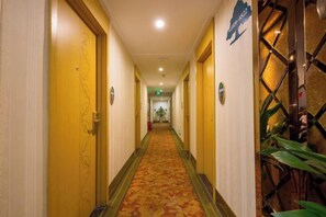 A hotel corridor with doors on both sides, a patterned carpet, and a plant on the right. - GreenTree Shell Hotel (Yiwu International Business City Changchun Accessories Specialty Street) (Yiwu)