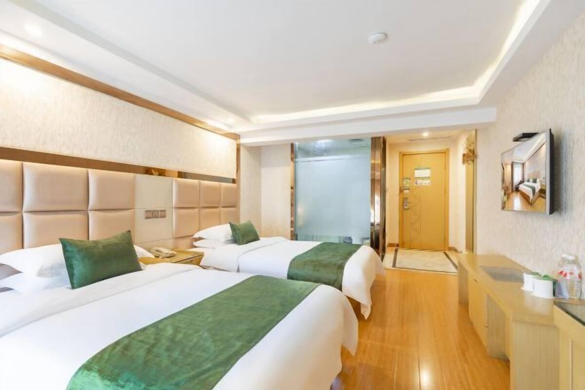 Une chambre d’hôtel avec deux lits, un plancher en bois, un téléviseur fixé au mur et une porte donnant sur la salle de bain.