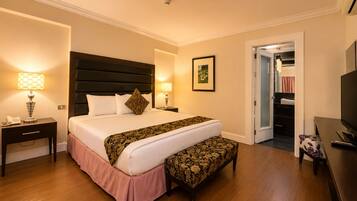 A hotel room with a large bed, bedside lamps, a bench, a TV, and a door leading to a closet.