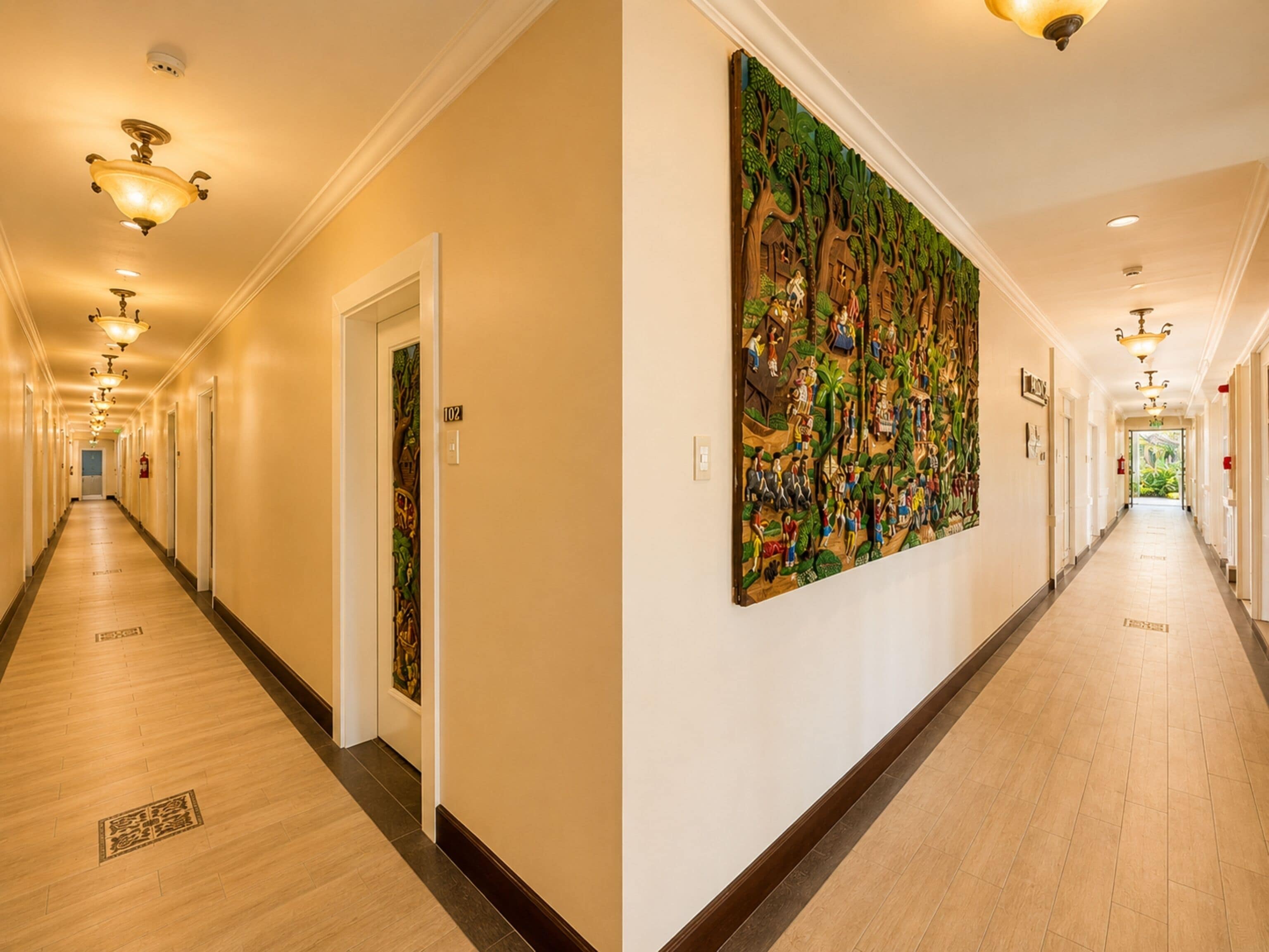 A long, well-lit hallway with wooden floors, doors, and a large colorful mural on the right wall.