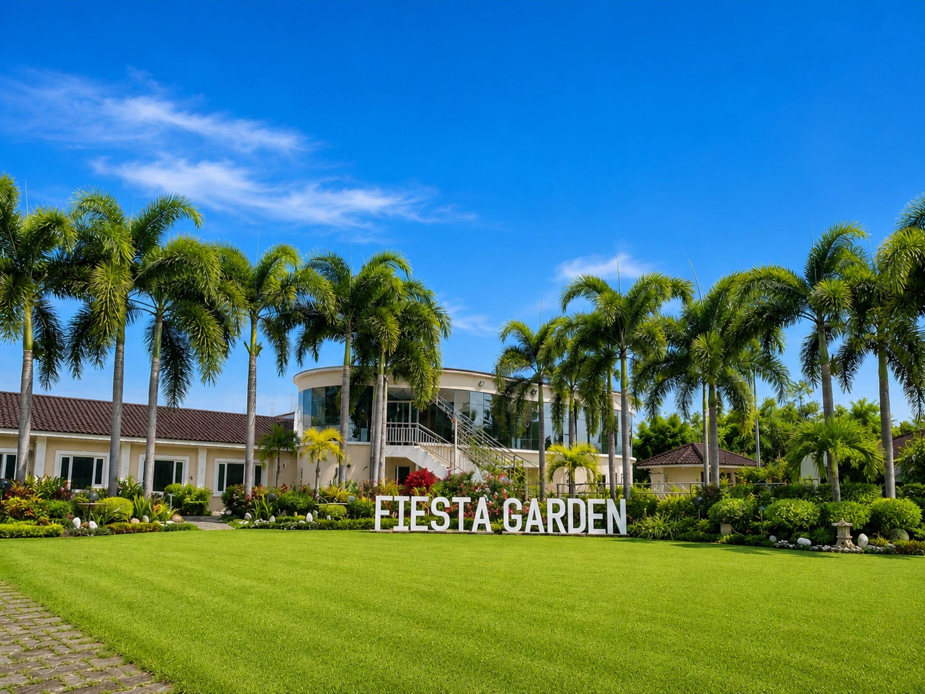 Un edificio moderno con fachada curva, rodeado de un jardín cuidado con palmeras y un cielo azul despejado.