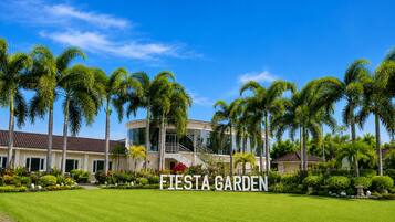 Un edificio moderno con fachada curva, rodeado de un jardín cuidado con palmeras y un cielo azul despejado.
