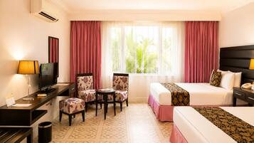Habitación de hotel con una cama, un escritorio con computadora, una silla, un televisor y una ventana con cortinas.