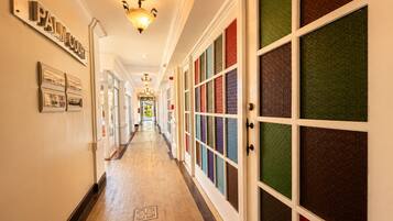 A hotel corridor with a 'PALM COURT' sign, a light fixture, and a row of doors with patterned glass panels.