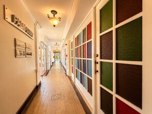 A hotel corridor with a 'PALM COURT' sign, a light fixture, and a row of doors with patterned glass panels.
