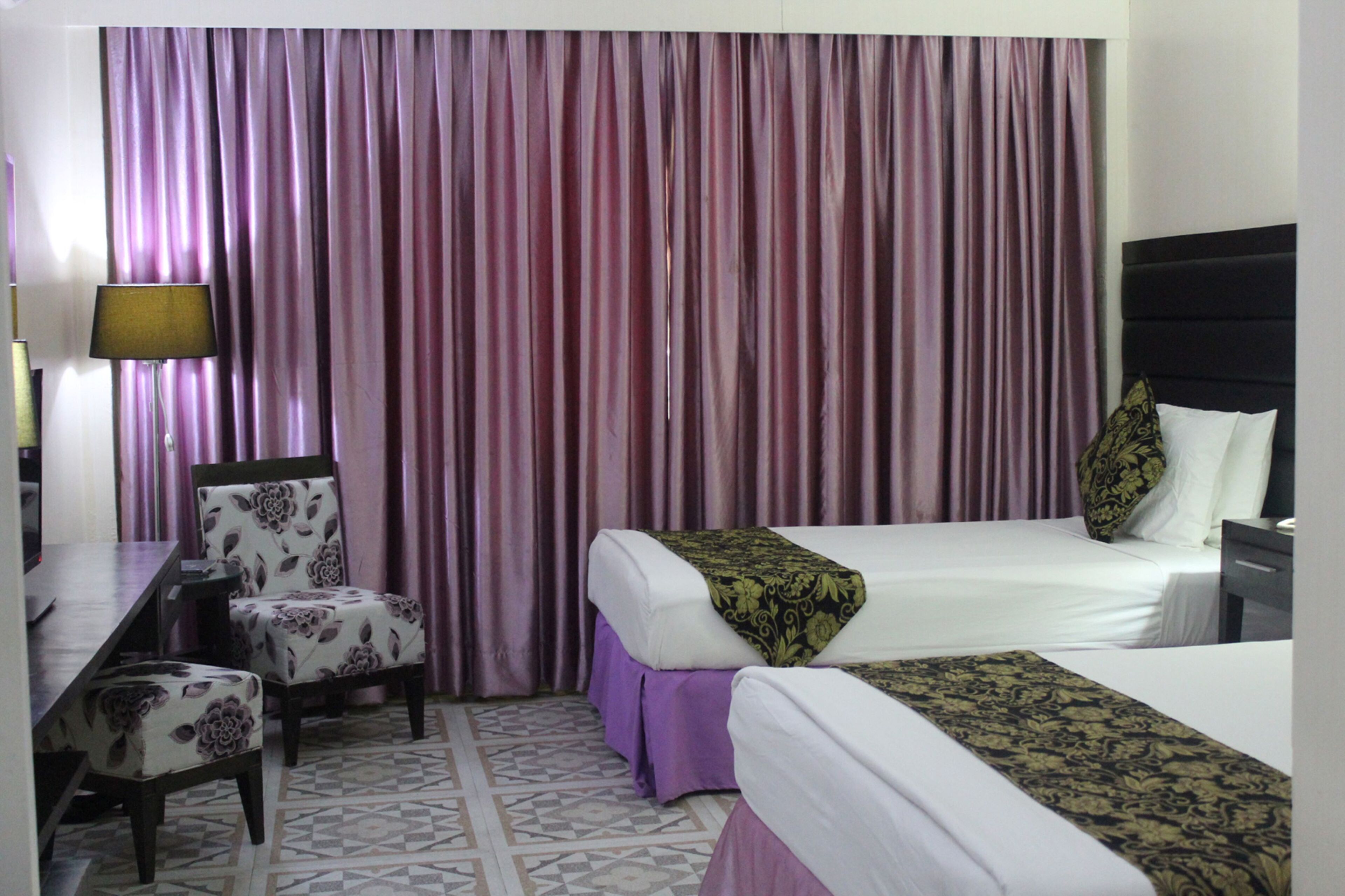 A hotel room with two beds, a desk, a chair, and a large window with curtains.