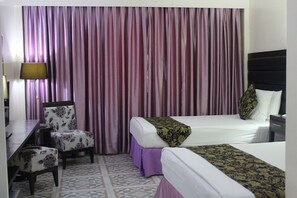 A hotel room with two beds, a desk, a chair, and a large window with curtains. - Fiesta Garden Hotel (Bantay)