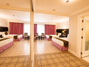 A hotel room with two beds, a dining table, chairs, a desk with a lamp, and a mirror. - Fiesta Garden Hotel (Bantay)