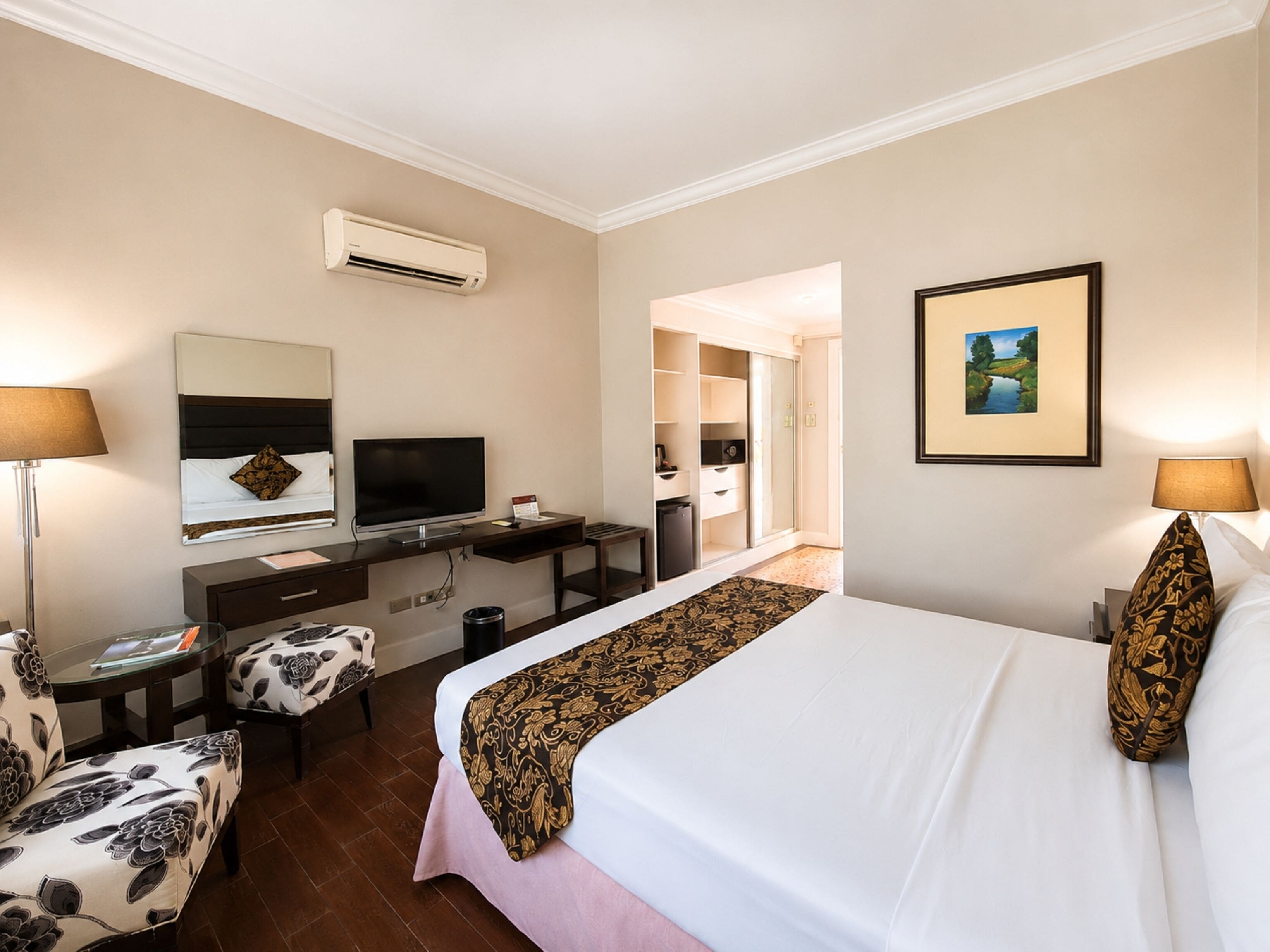A hotel room with a bed, desk, chair, TV, and wardrobe.