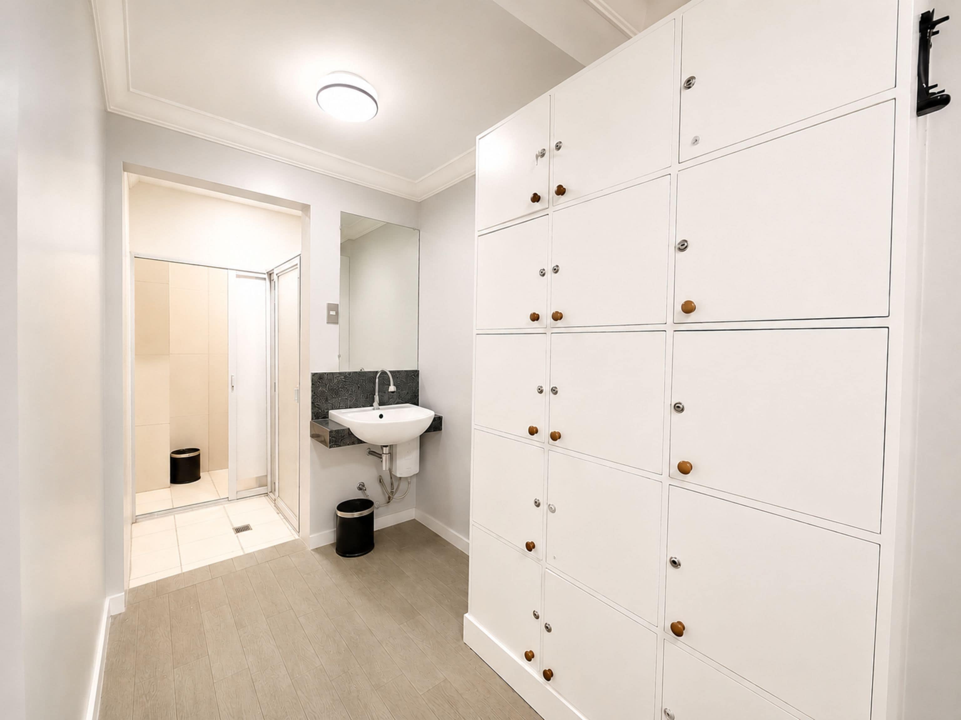 Un couloir avec un espace de casiers blancs, un lavabo et une poubelle.