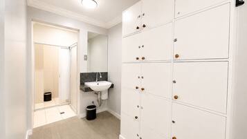 Un couloir avec un espace de casiers blancs, un lavabo et une poubelle.
